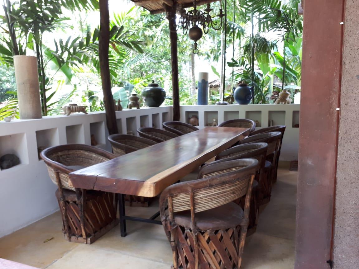 Comedor con mesa larga de madera y sillas de equipal, abierto a la selva.